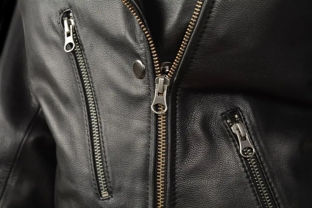 Close-up of a black leather jacket featuring silver zippers and a snap button.