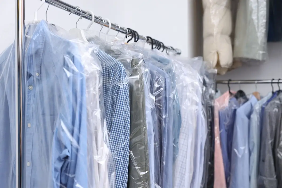 A row of shirts in various colors and patterns hangs on a rack, each covered with a clear plastic garment bag after professional dry cleaning Manlius service.