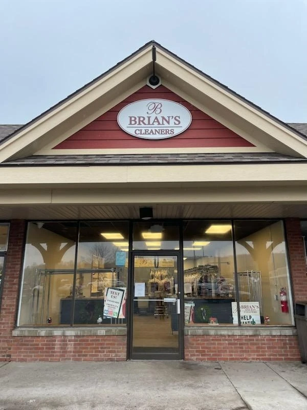 Storefront of Brian’s Cleaners with a glass entrance, red and white sign above, and dry cleaning items visible inside.