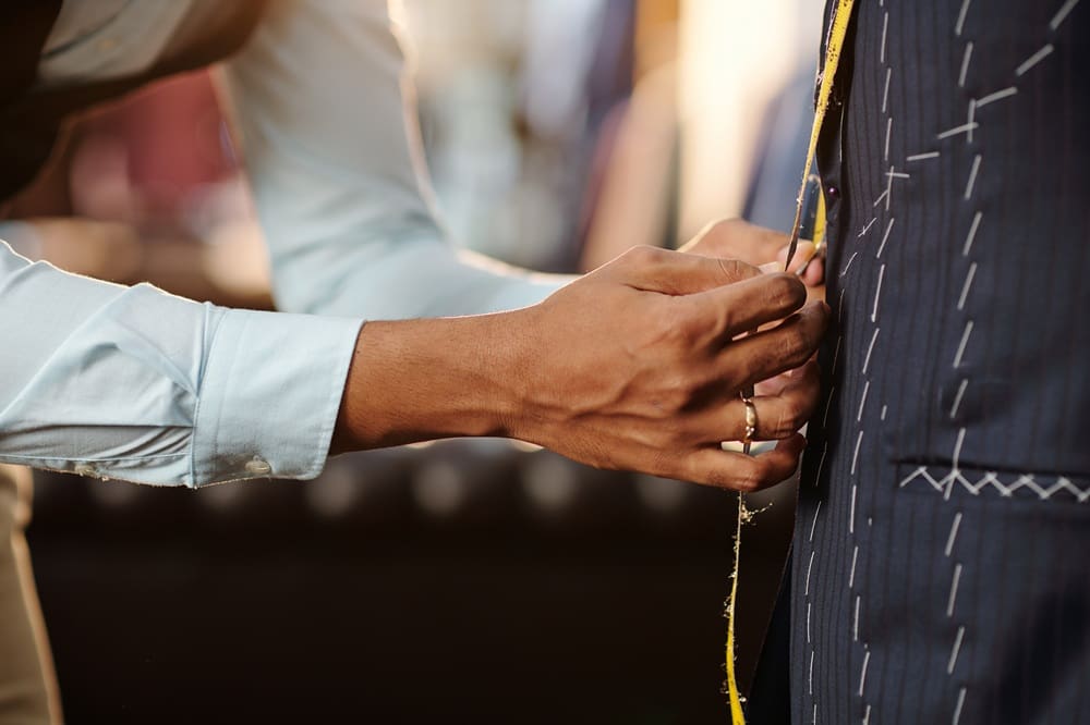 A tailor measures a person wearing a pinstripe suit with a yellow tape measure.