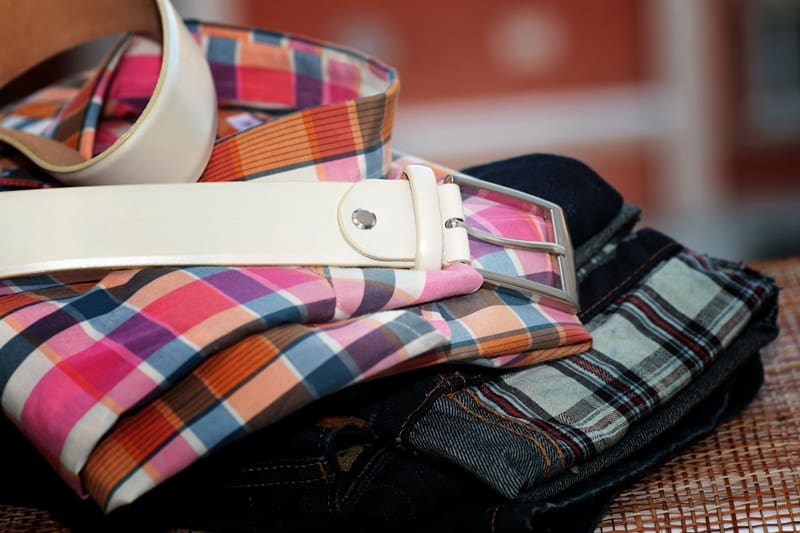 A white belt placed on top of folded plaid shirts and dark jeans.
