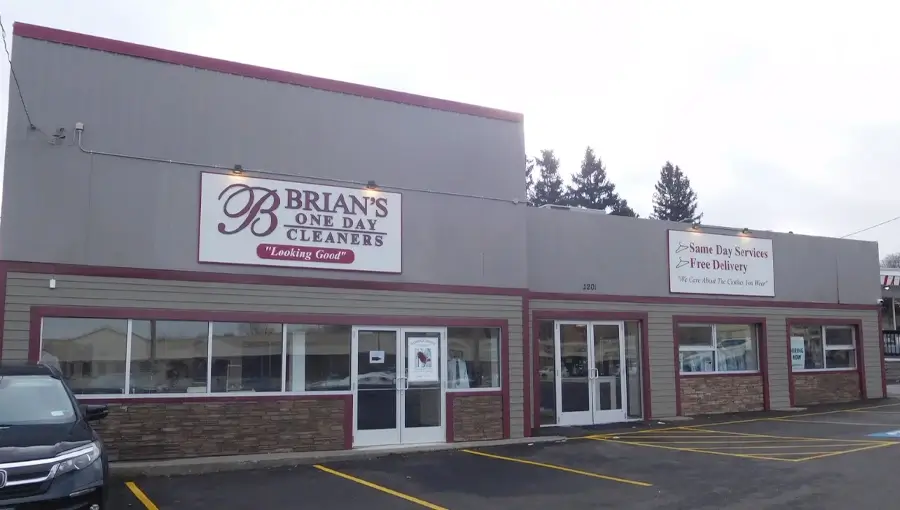 The exterior of Brian’s One Day Cleaners, a dry cleaning business, with a sign advertising same day services and several parking spaces in front.